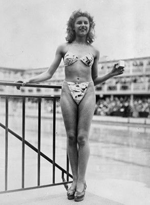 The new 'Bikini' swimming costume (in a newsprint-patterned fabric), which caused a sensation at a beauty contest at the Molitor swimming pool in Paris. Designer Louis Reard was unable to find a 'respectable' model for his costume and the job of displaying it went to 19-year-old Micheline Bernardini, a nude dancer from the Casino de Paris. She is holding a small box into which the entire costume can be packed. Celebrated as the first bikini, Luard's design came a few months after a similar two-piece design was produced by French designer Jacques Heim. (Photo by Keystone/Getty Images)