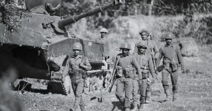 1971 भारत-पाकिस्तान युद्ध के दौरान एक बर्बाद हो चुके टैंकर के सामने से गुज़रते भारतीय सैनिक.