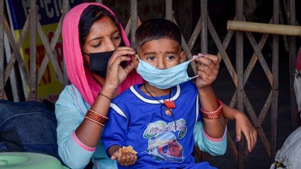 बाहर निकलते वक्त मास्क पहनना जरूरी है. ऐसे में एक महिला अपने बच्चे को मास्क पहनाते हुए. (Photo: PTI)