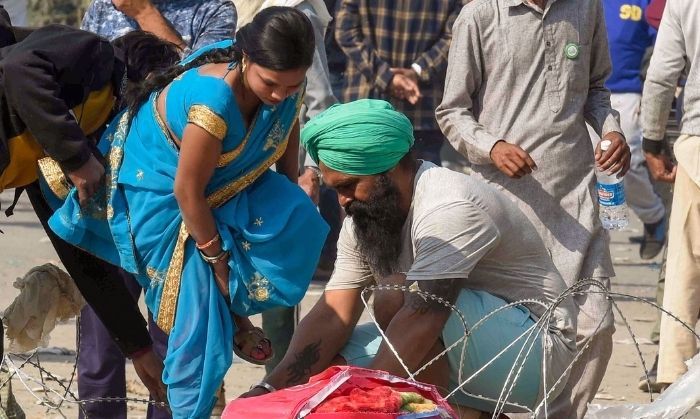 'दिल्ली चलो' मार्च के दौरान सिंघू सीमा पर एक अस्थायी अवरोधक पार करवाने में एक महिला की मदद करता हुआ एक किसान. 29 नवंबर, 2020. (पीटीआई/अतुल यादव)